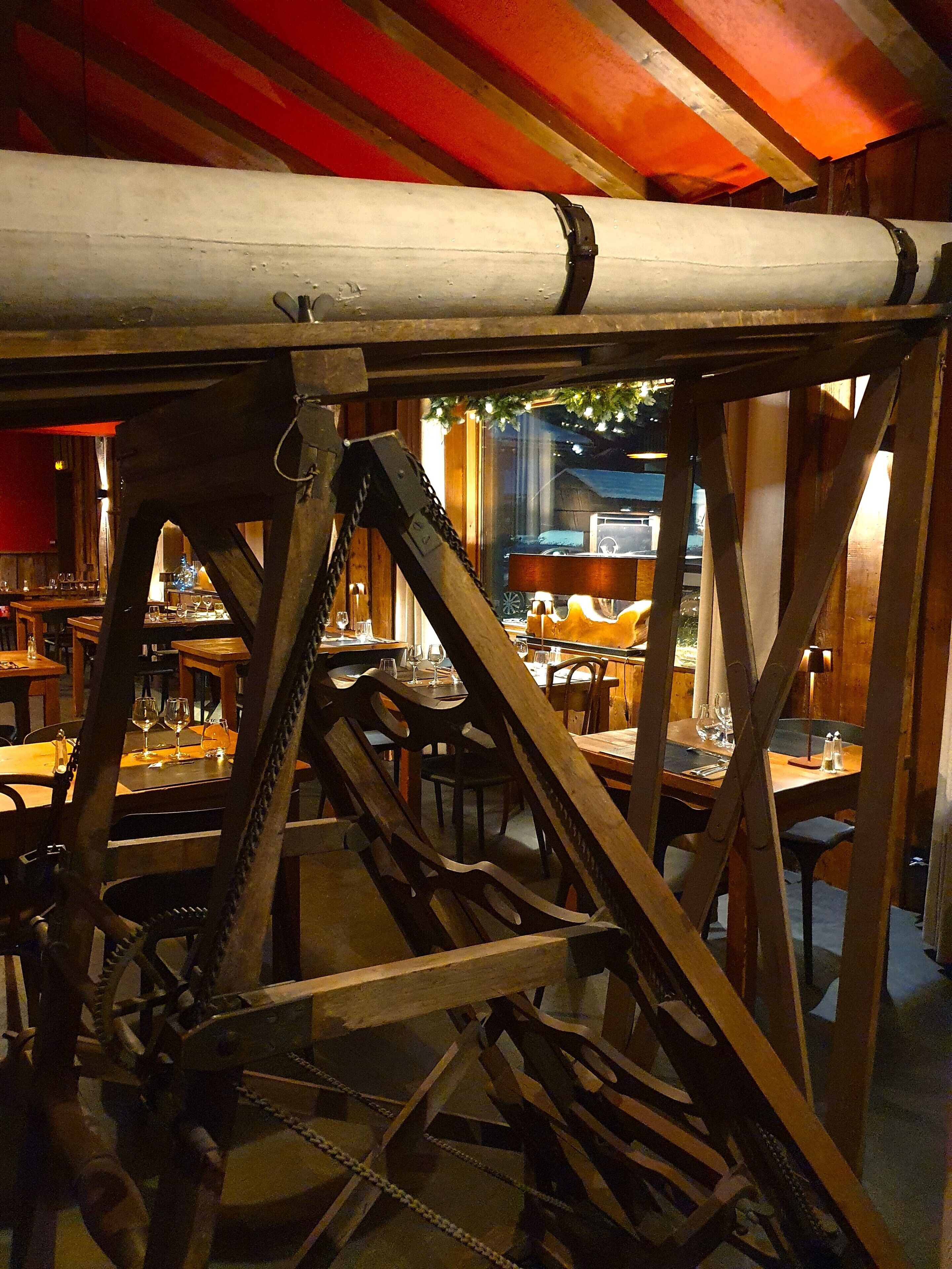 A dining area with wooden tables and chairs, a large white pipe, and a chain mechanism.