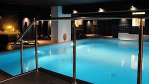 An indoor swimming pool with a glass barrier, a stone sculpture, and a modern ceiling light fixture. - Chalet Hotel Du Bois (Les Houches)