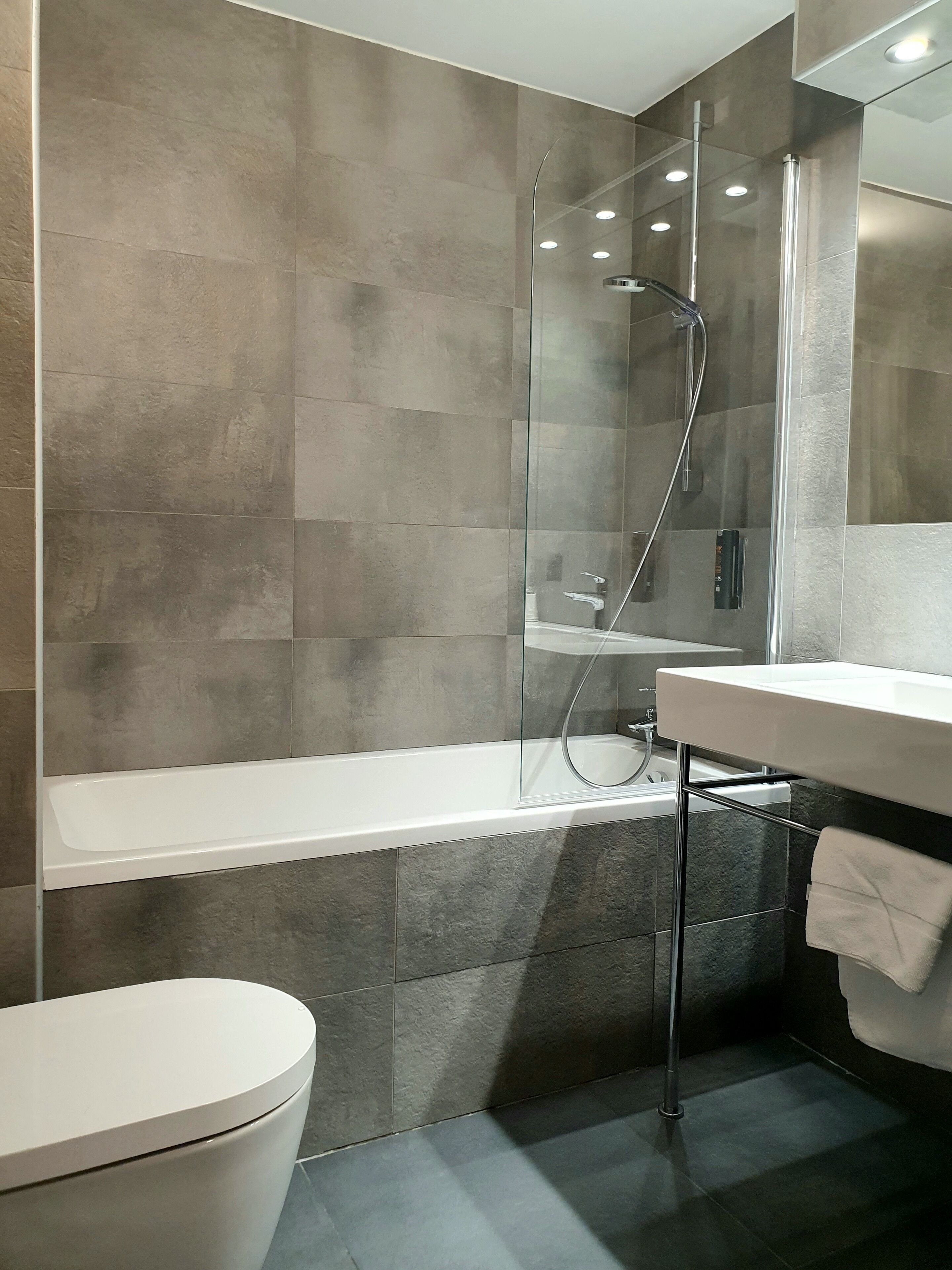 Ein modernes Badezimmer mit einer gläsernen Duschkabine, einer weißen Badewanne und einem weißen Waschbecken. Ein Handtuch hängt an der Wand.