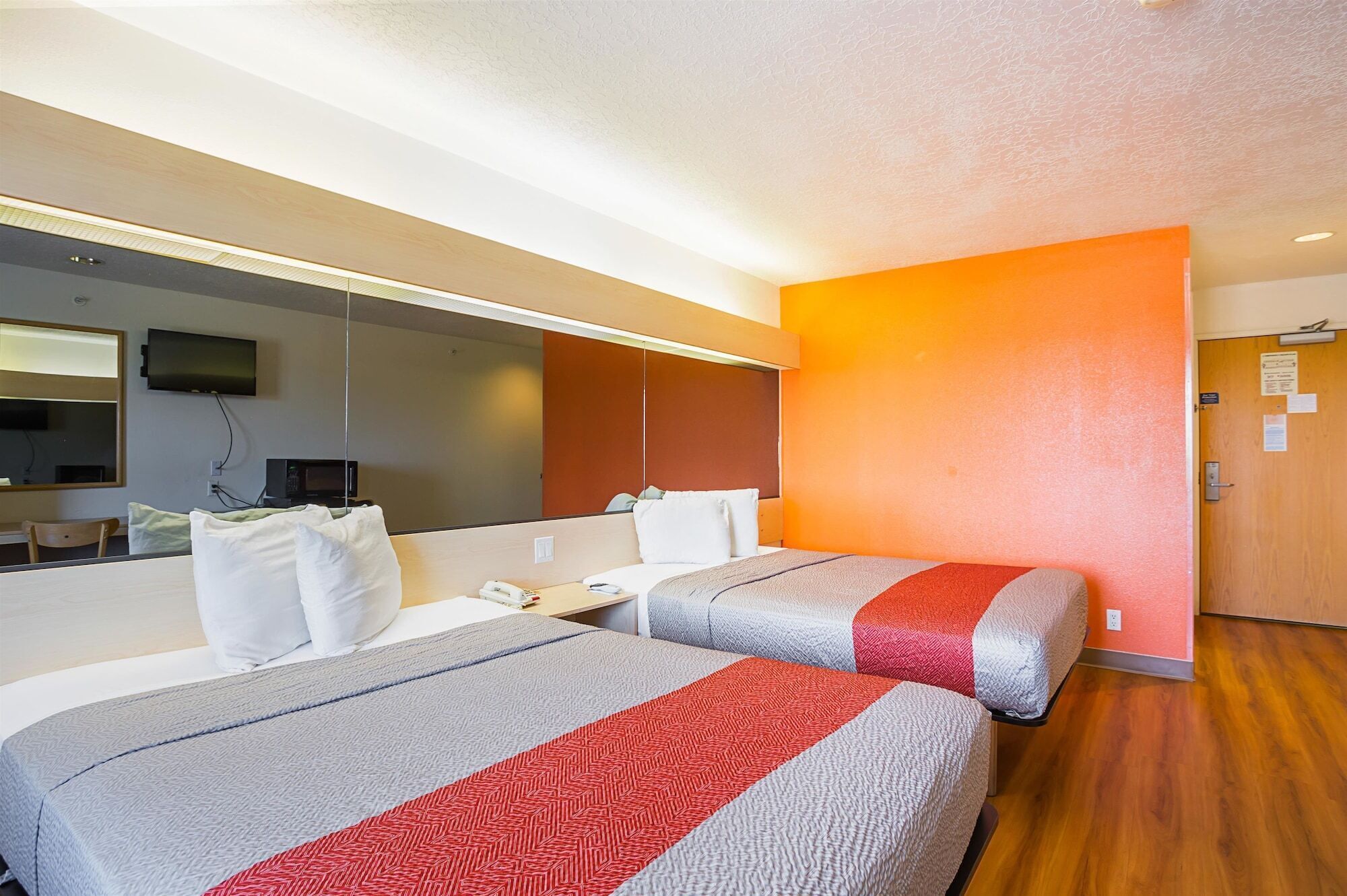 A hotel room with two beds, a TV, a desk, and a mirror.