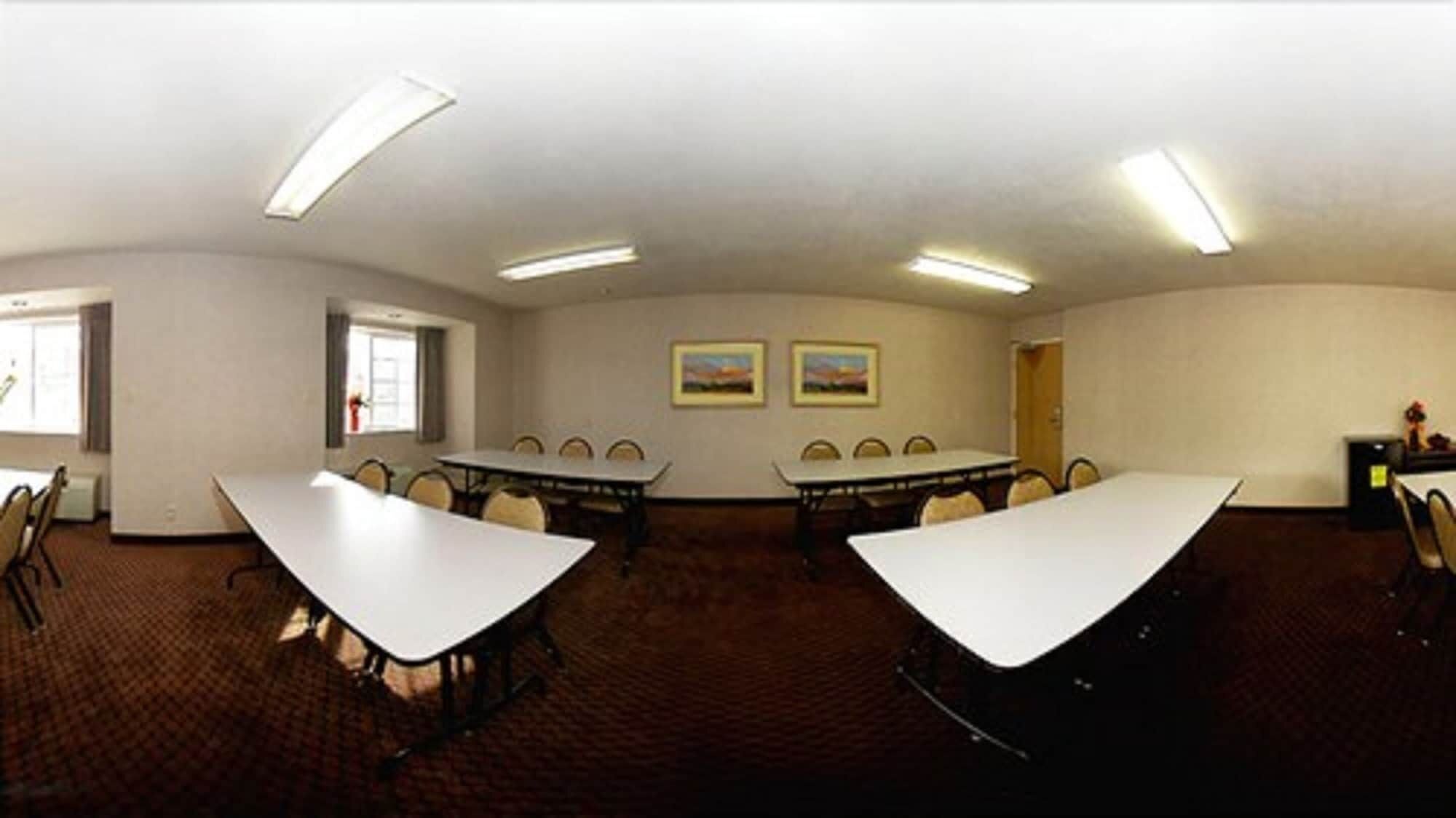 A conference room with two large tables, chairs, ceiling lights, and two framed pictures on the wall.