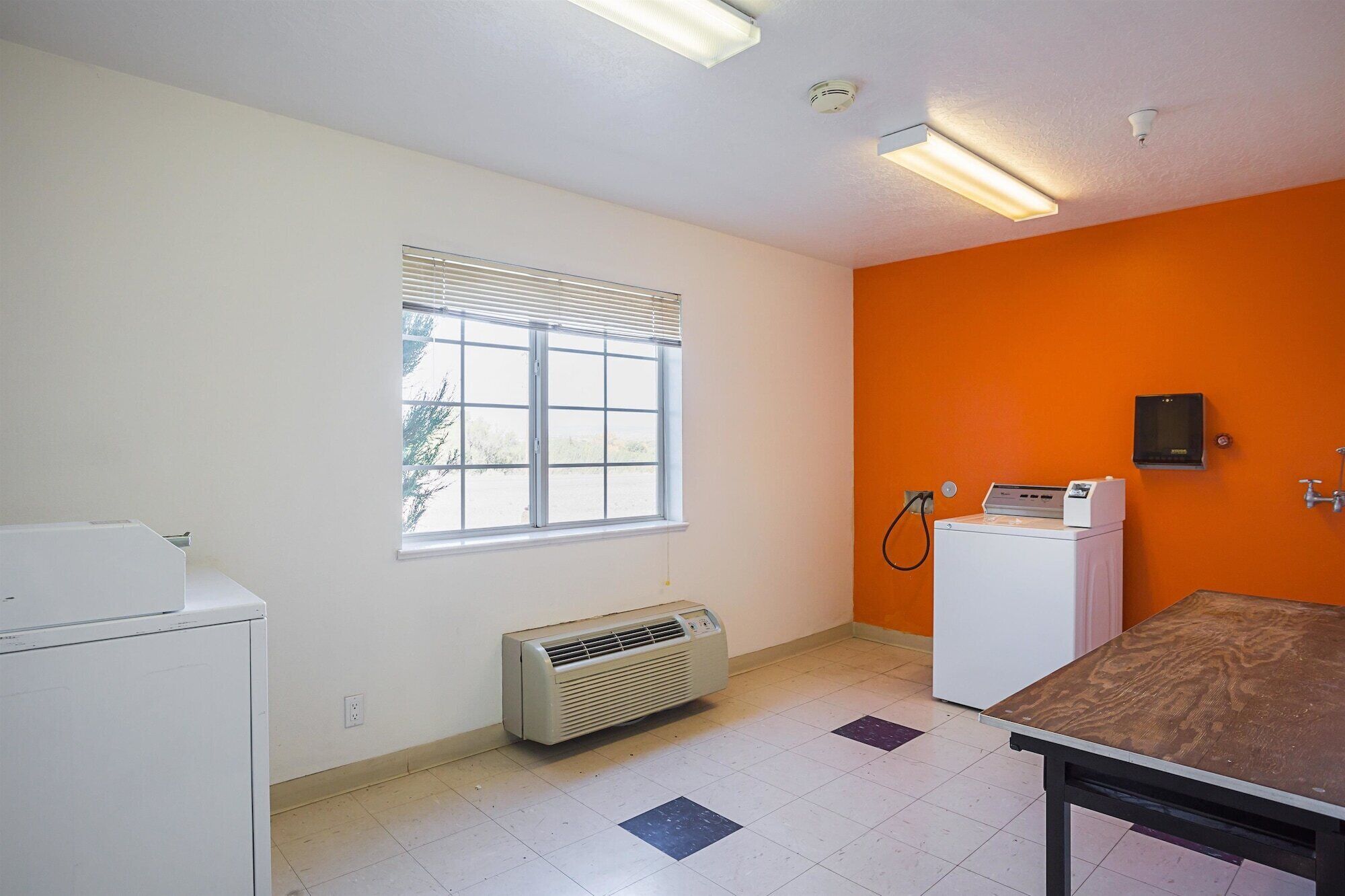 A room with a window, an air conditioning unit, a washing machine, and a table.