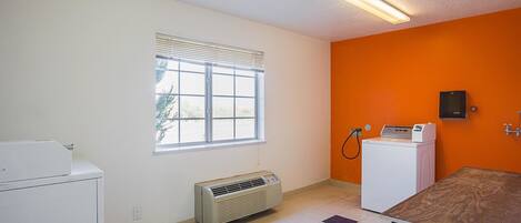 A room with a window, an air conditioning unit, a washing machine, and a table.