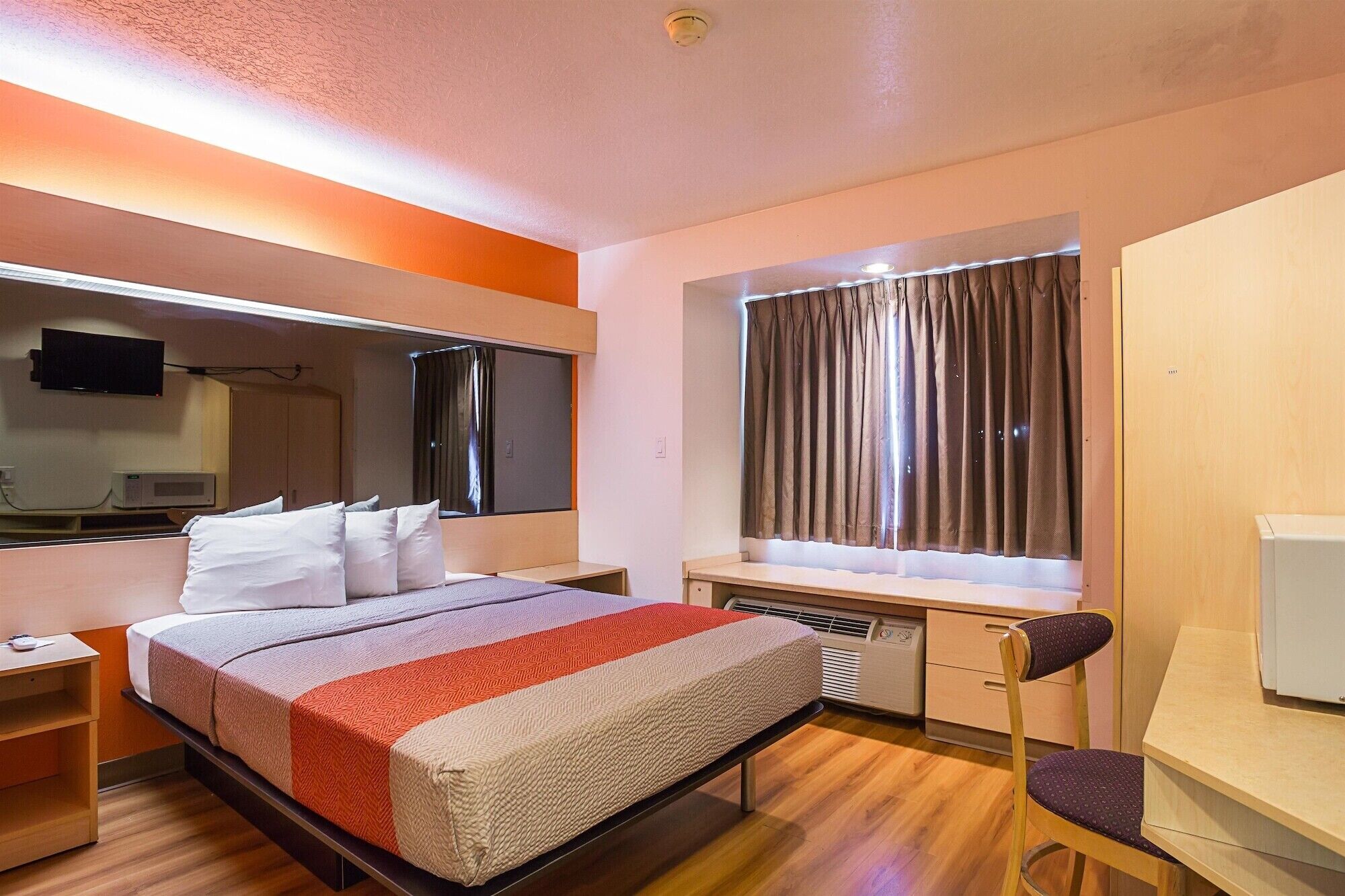 A hotel room with a bed, a desk, a chair, a television, and a window with curtains.