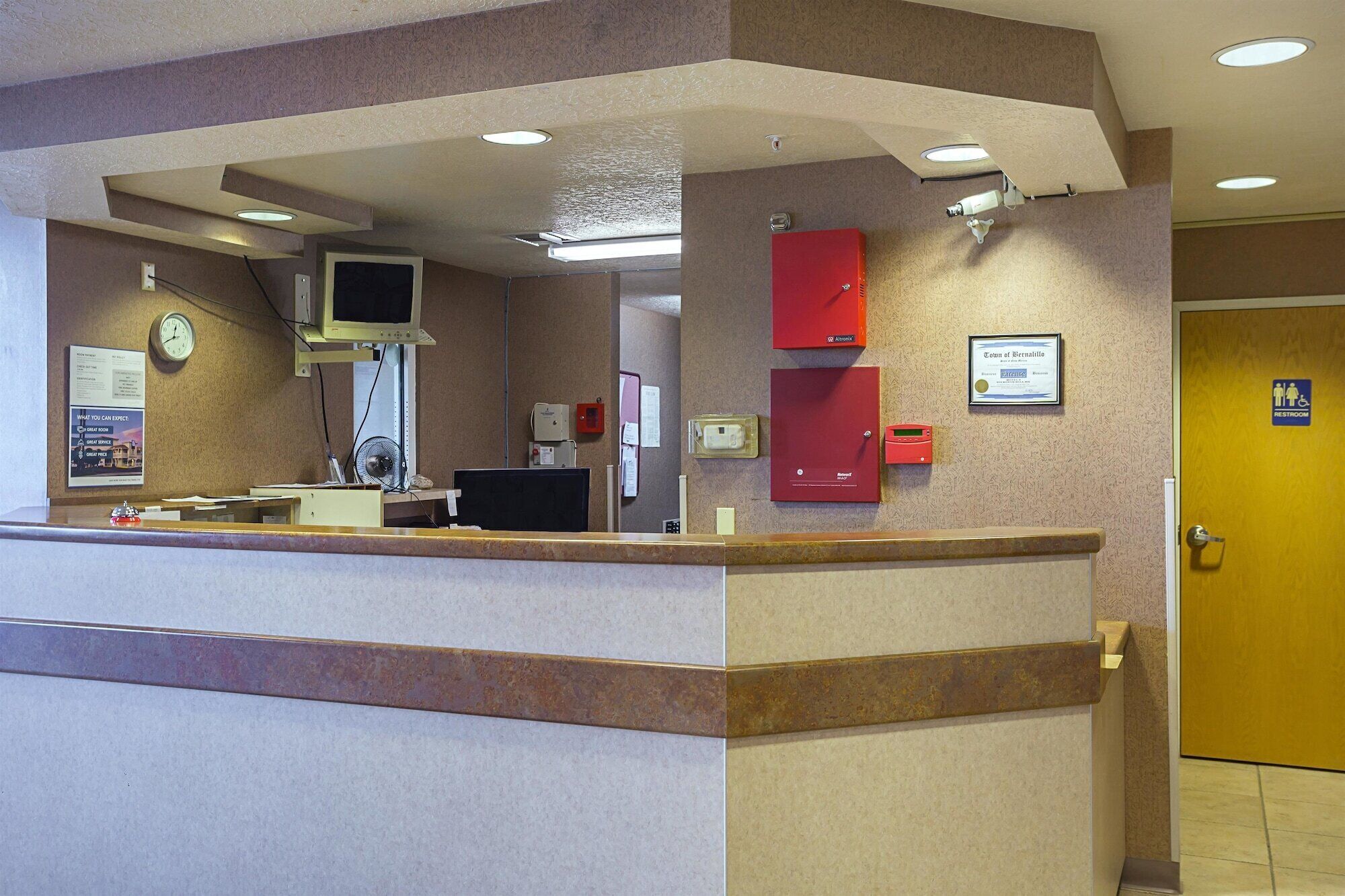 A reception area with a counter, a clock, a computer monitor, and a framed certificate on the wall.