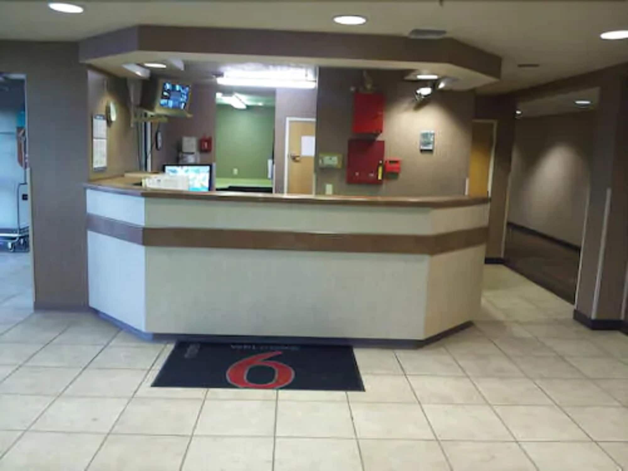 A reception desk with a digital screen, a fire extinguisher, and a red emergency phone.