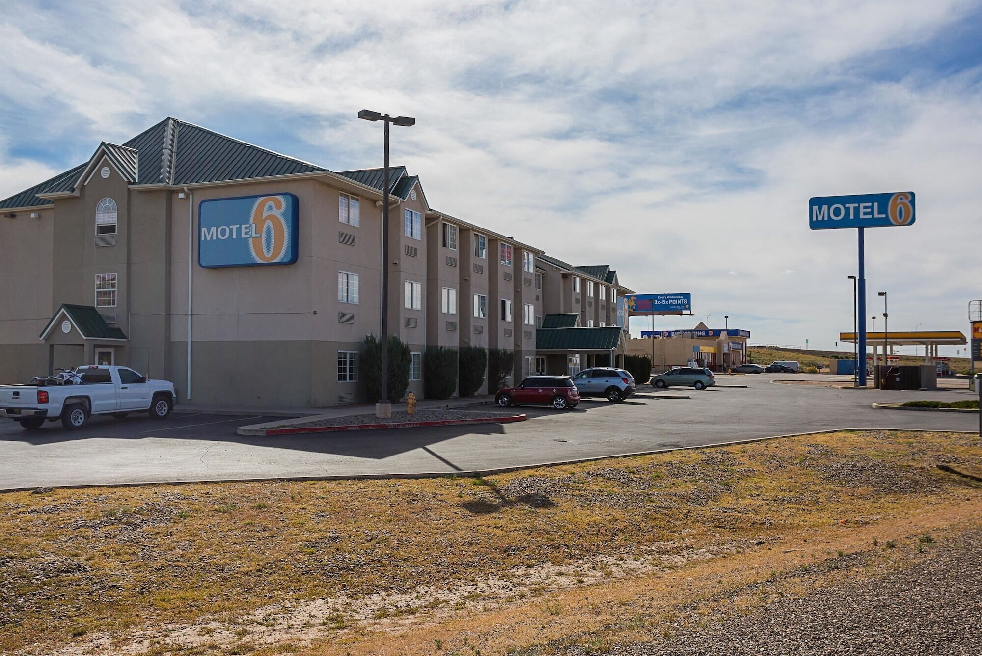A Motel 6 building with a parking lot, a gas station, and a few vehicles parked in front.