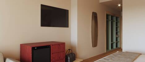 Una habitación de hotel con una cama, un mueble de madera con televisor, un escritorio pequeño, un espejo montado en la pared y un estante verde.