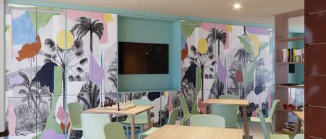Une salle de jeux pour enfants avec des œuvres d’art abstraites et colorées sur les murs, un téléviseur à écran plat, ainsi que plusieurs tables et chaises.