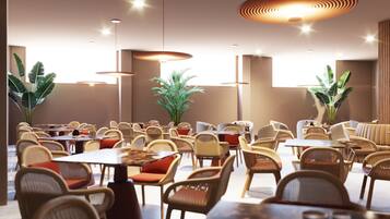 Un restaurante amplio con techos altos, varias mesas para comer, sillas de mimbre y grandes macetas con plantas.