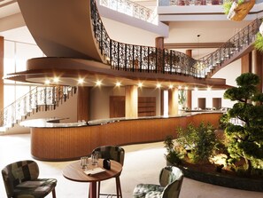 Un hall d’hôtel moderne avec un comptoir d’accueil incurvé, un espace salon et un escalier agrémenté de rampes décoratives.