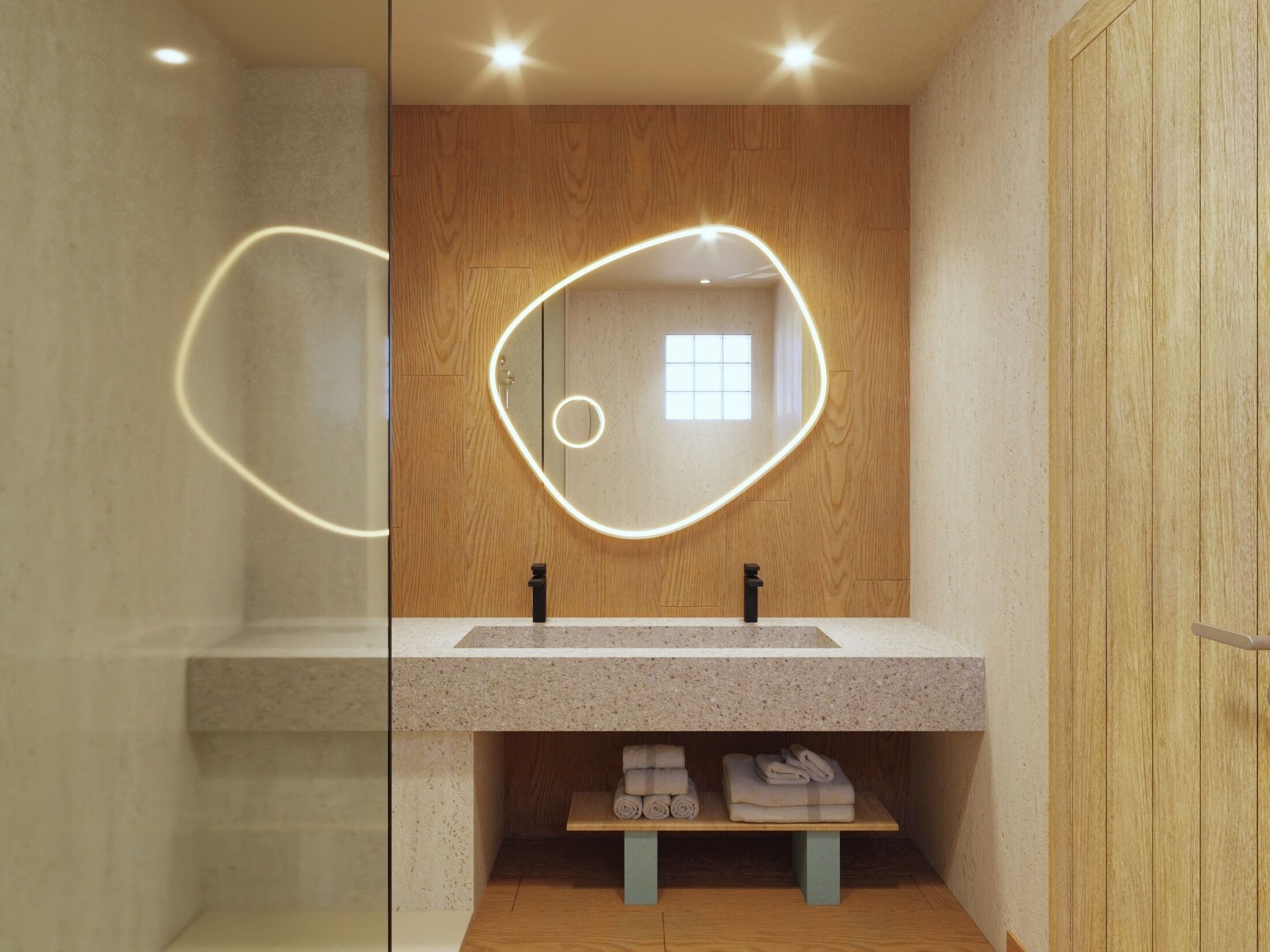 Un baño moderno con tocador de madera, espejo con iluminación perimetral y repisa con toallas dobladas.