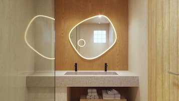 Un baño moderno con tocador de madera, espejo con iluminación perimetral y repisa con toallas dobladas.