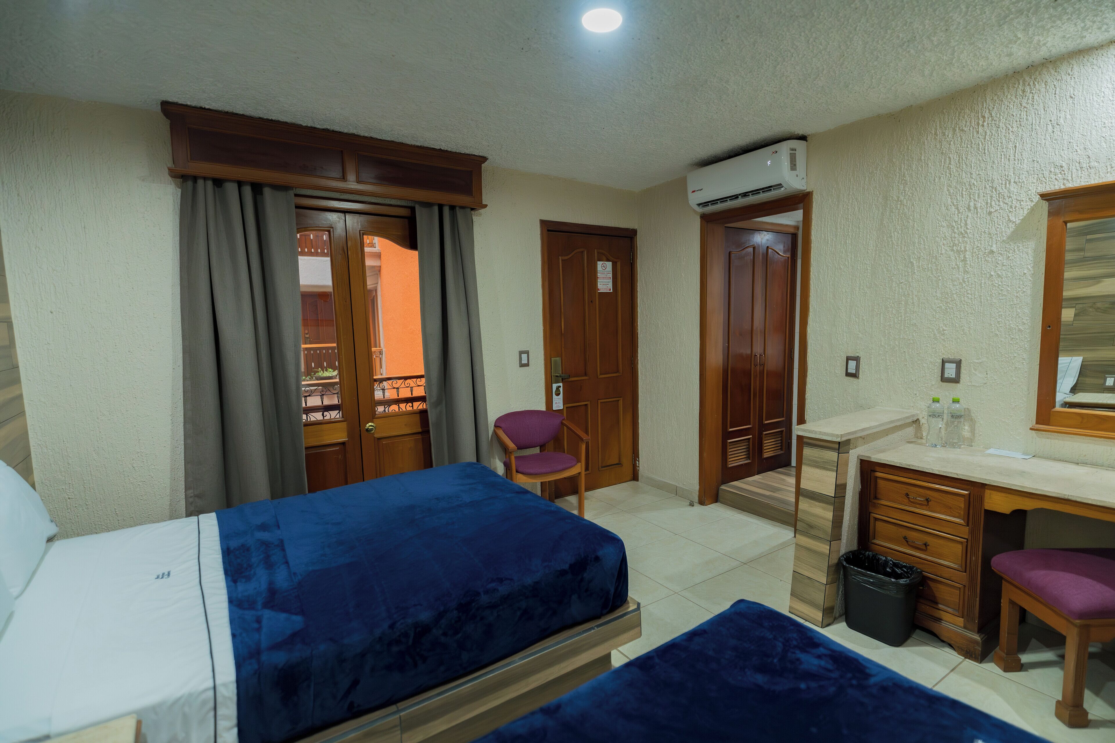Habitación de hotel con dos camas, un escritorio, una silla, un cesto de basura y un aire acondicionado.