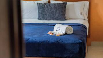 A neatly made bed with a blue bedspread and a rolled towel with text.