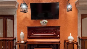 A room with a wooden piano, a television mounted on the wall, and multiple hanging lanterns.