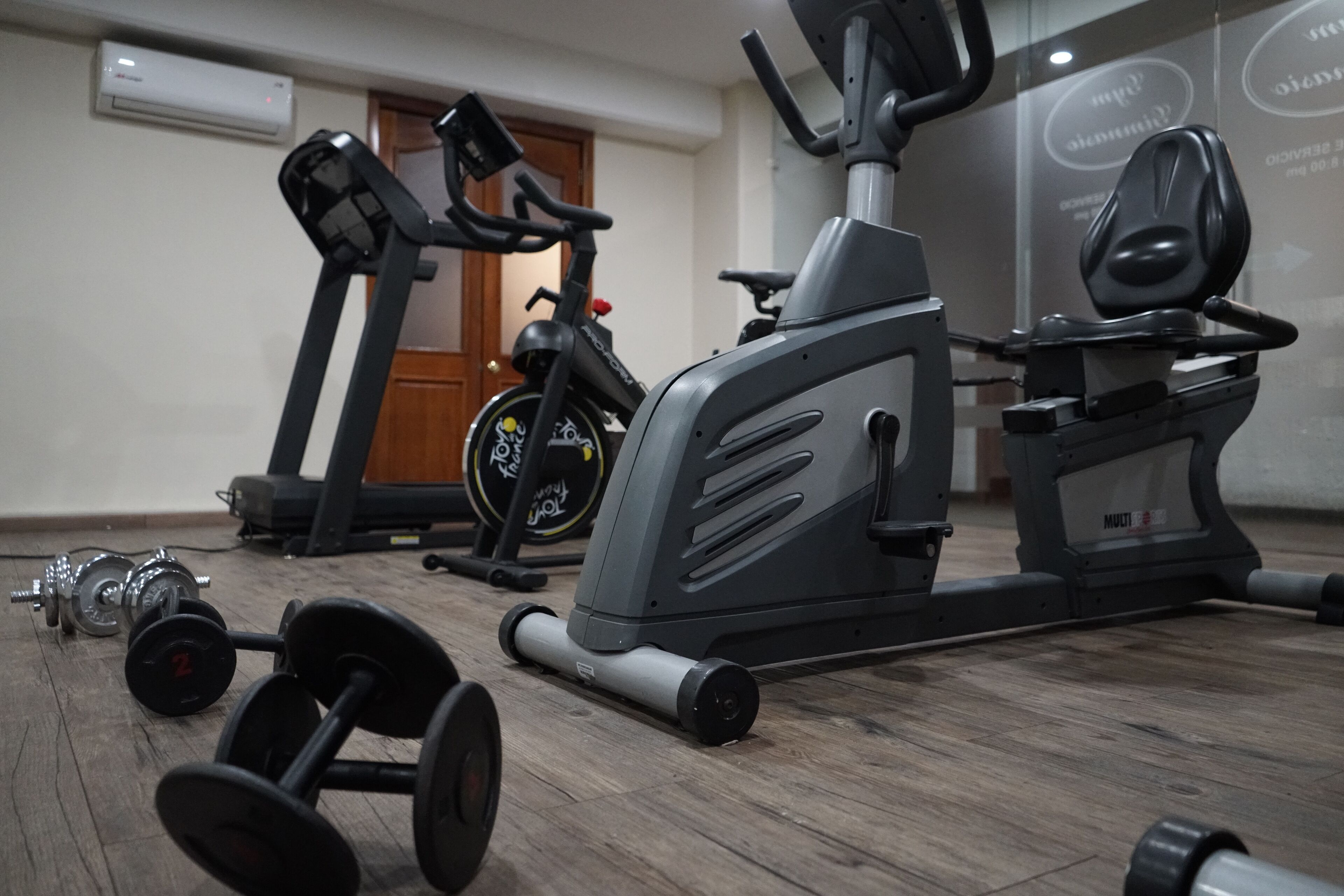 Un gimnasio con equipo de ejercicio, incluyendo una cinta de correr, bicicleta estática y mancuernas.