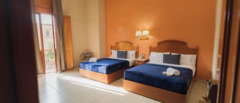 Habitación de hotel con dos camas, una mesita de noche, una lámpara y vistas al exterior.
