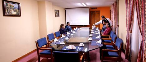 A conference room with a glass table, blue chairs, and a projector screen.