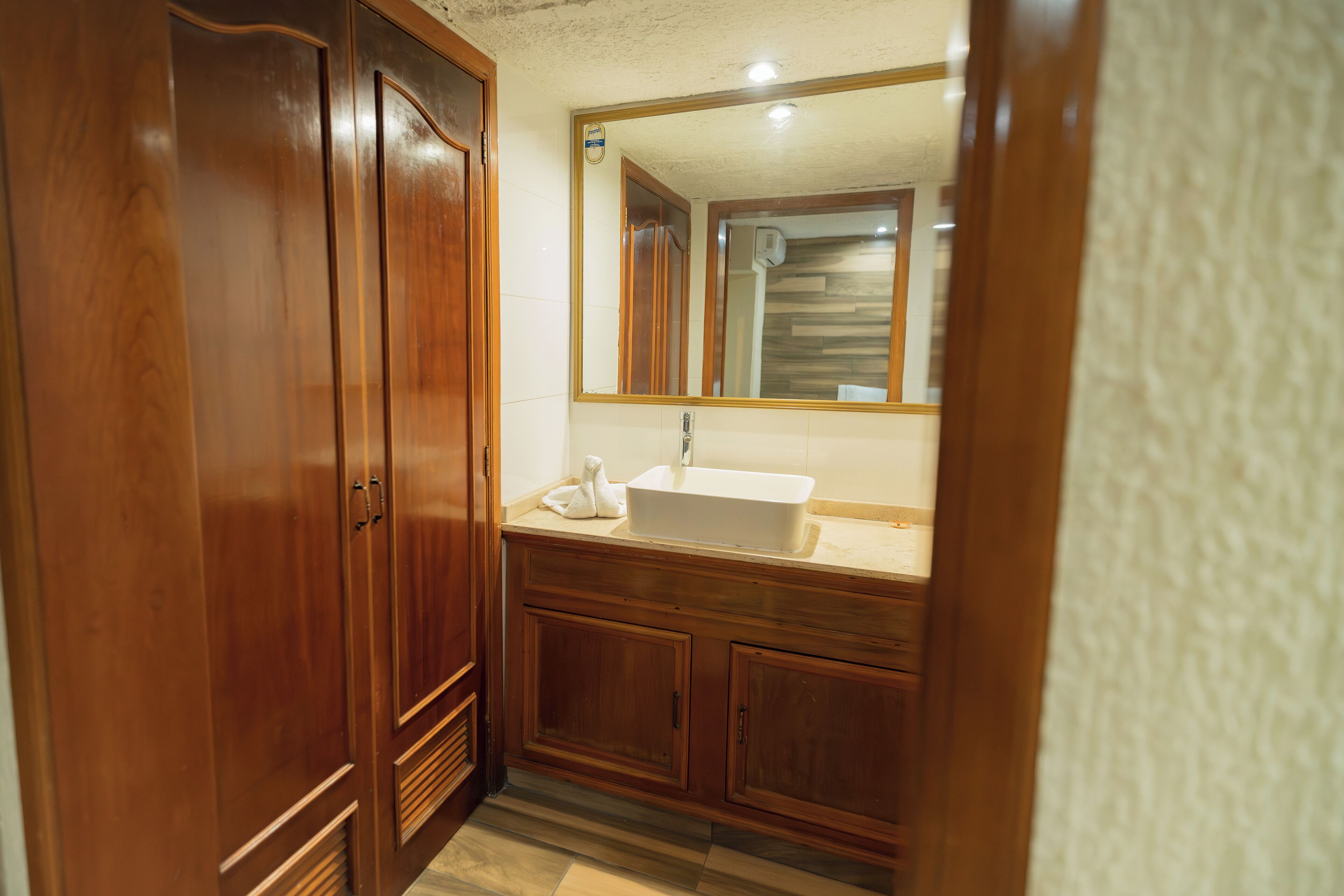 Un baño con armarios de madera, un lavabo blanco y un espejo sobre él.