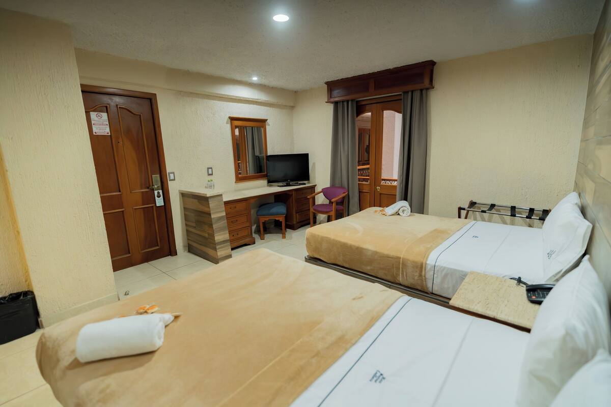 A hotel room with two beds, a desk, a chair, a television, and a wardrobe.