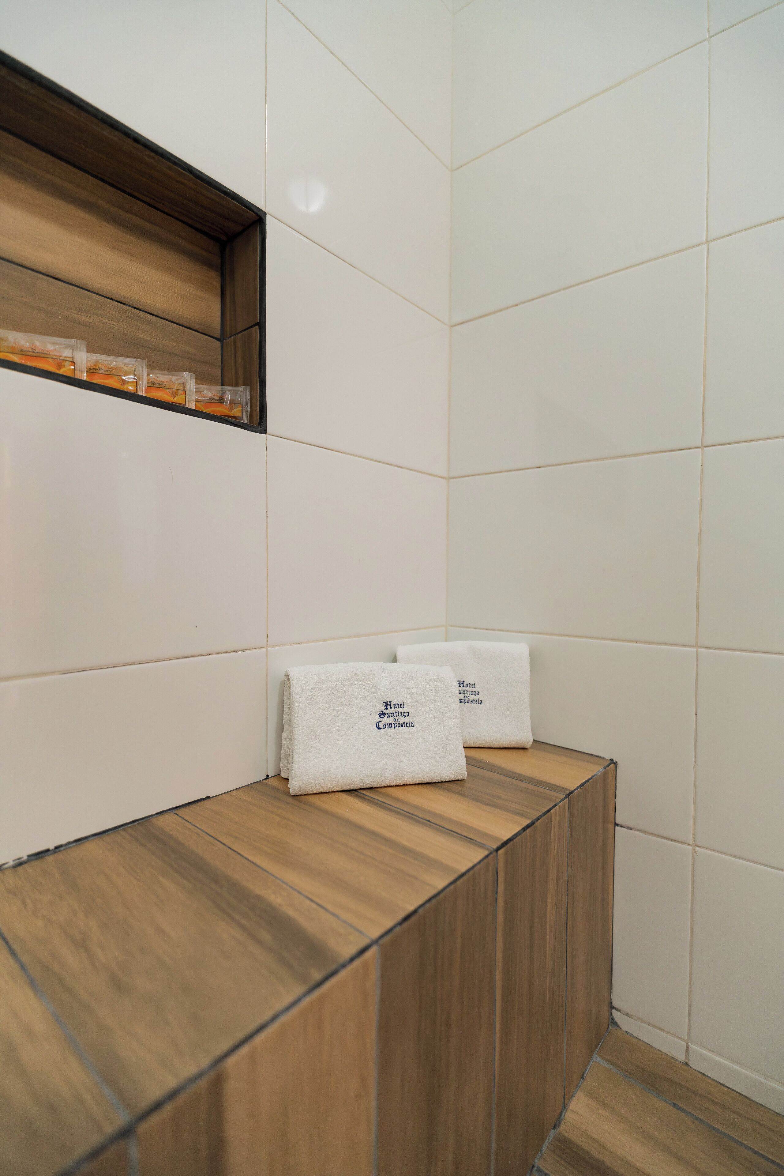Un coin d’une chambre d’hôtel avec un banc en bois et deux serviettes blanches ornées d’un motif.