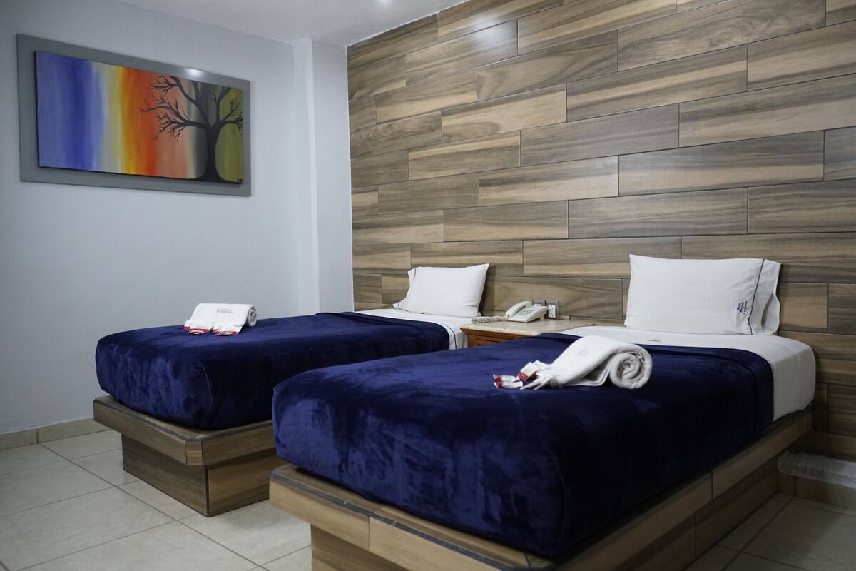 A hotel room with two beds, wooden headboard, and a painting on the wall.