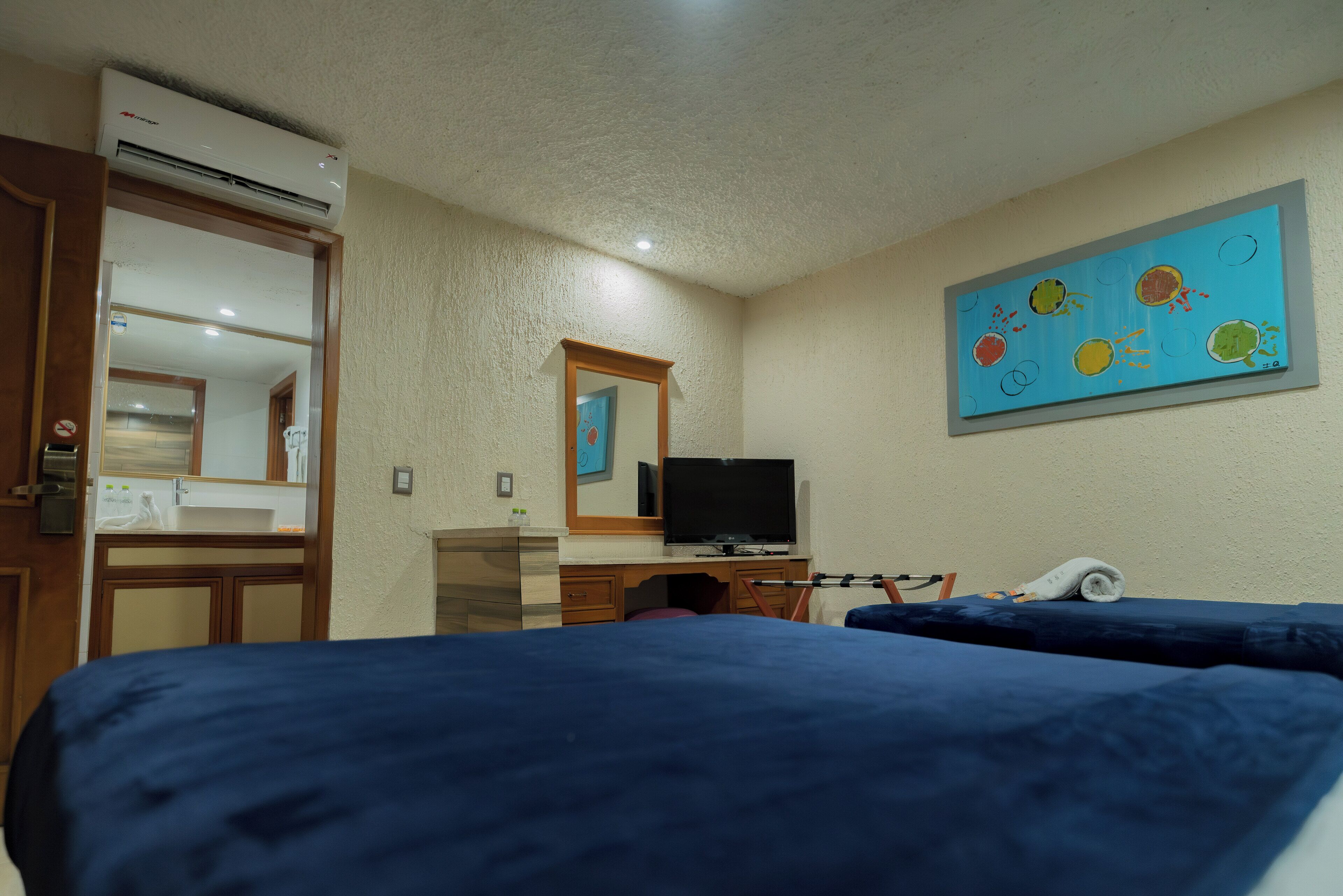 Habitación de hotel con dos camas, televisión, baño con espejo y un cuadro en la pared.