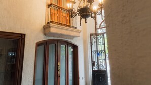A spacious hallway with a high ceiling, ornate ceiling details, a chandelier, and a large wooden door.