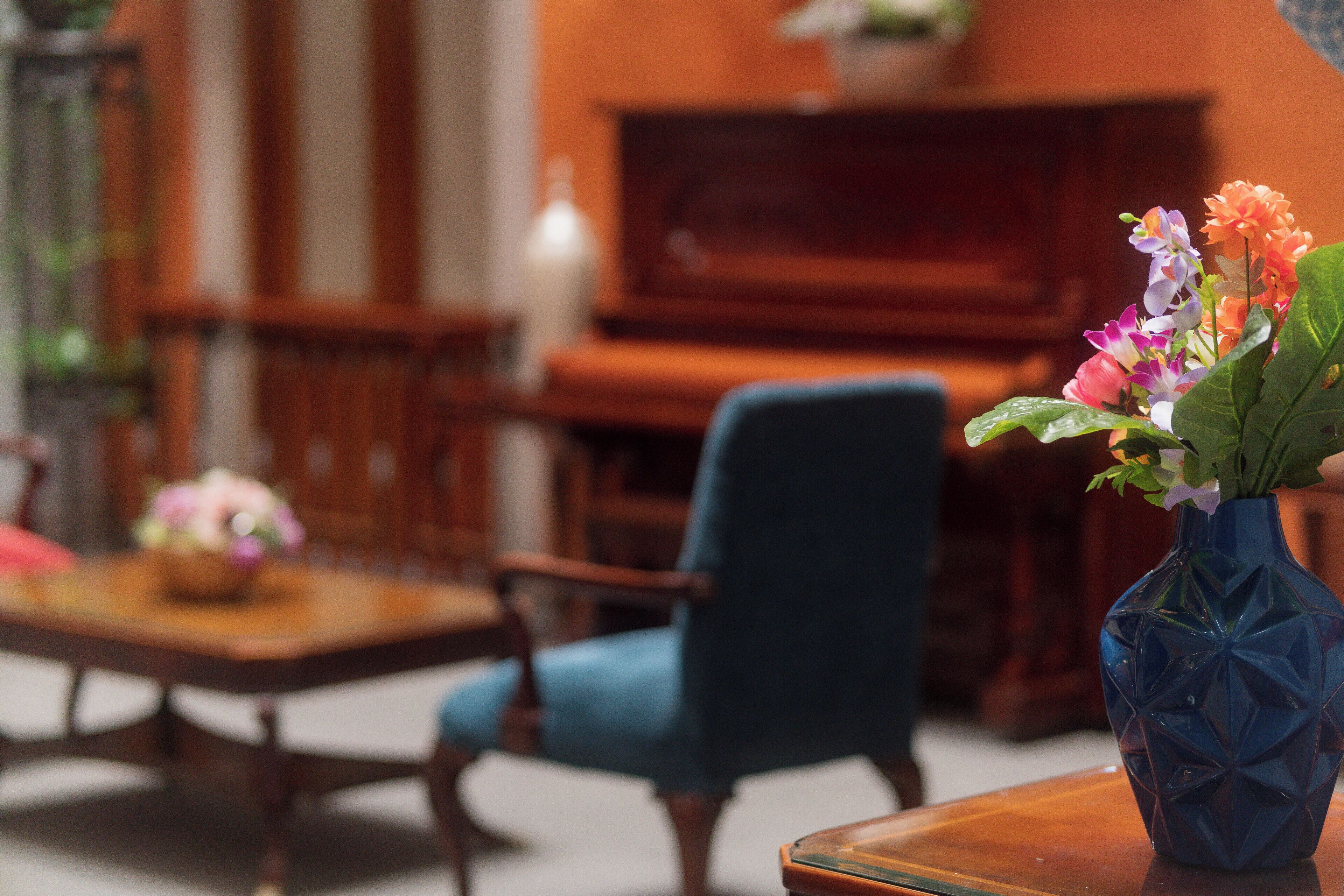 A room with a blue armchair, a wooden coffee table with a vase of flowers, and a television in the background.