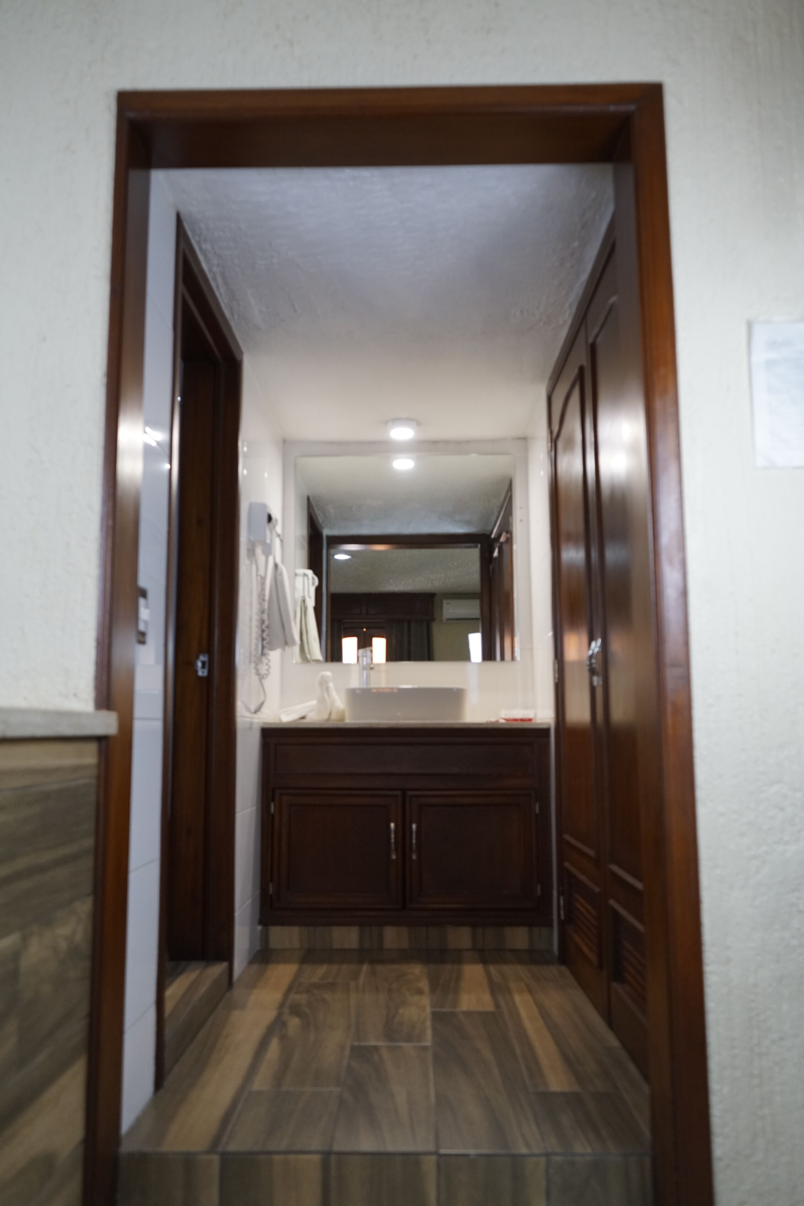 Un estrecho pasillo que conduce a un baño con tocador de madera, un espejo y un lavabo.