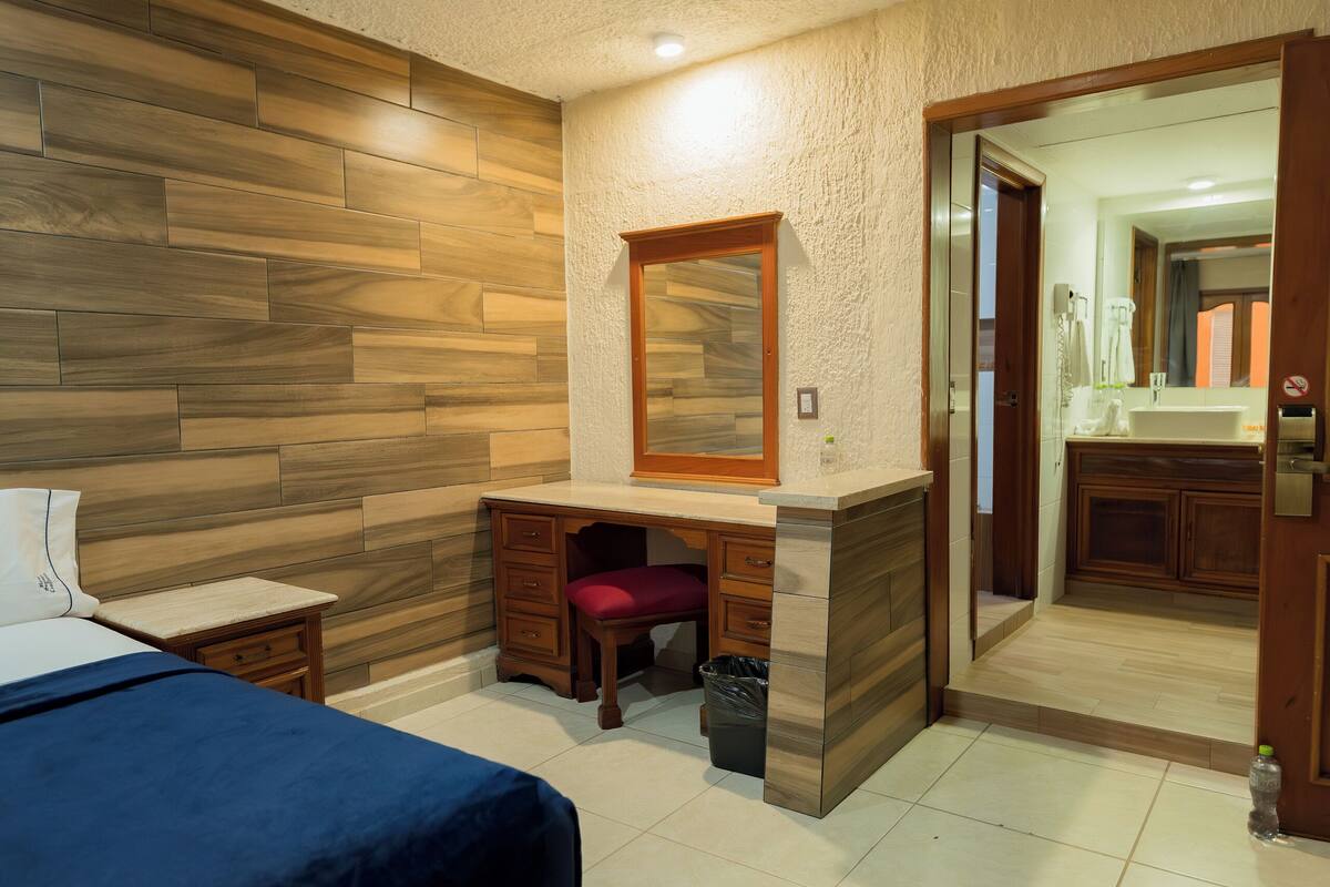 A bedroom with a bed, a desk, and a mirror.