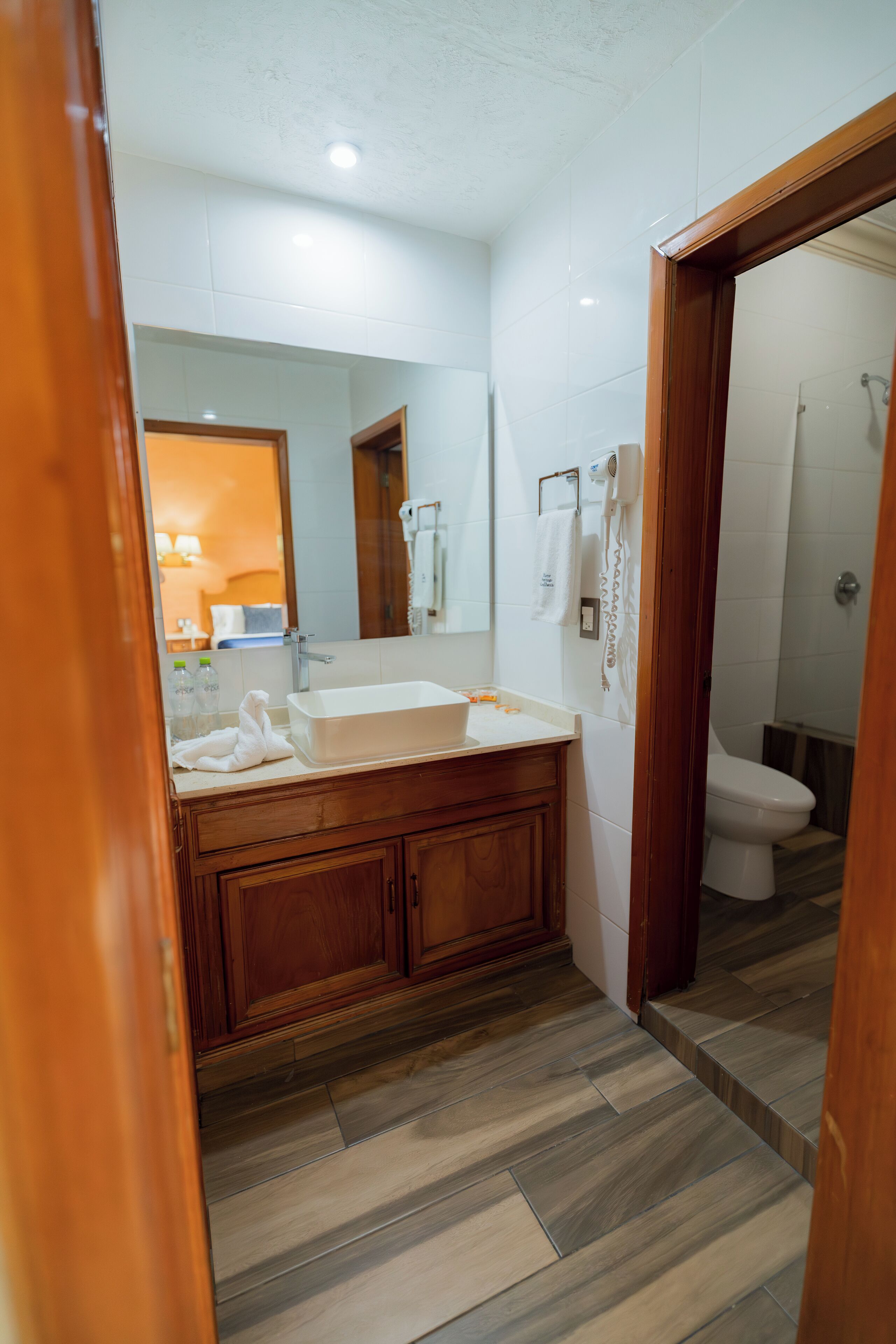 Une salle de bain avec un meuble-lavabo en bois, un lavabo blanc et un miroir. On aperçoit une douche au fond.