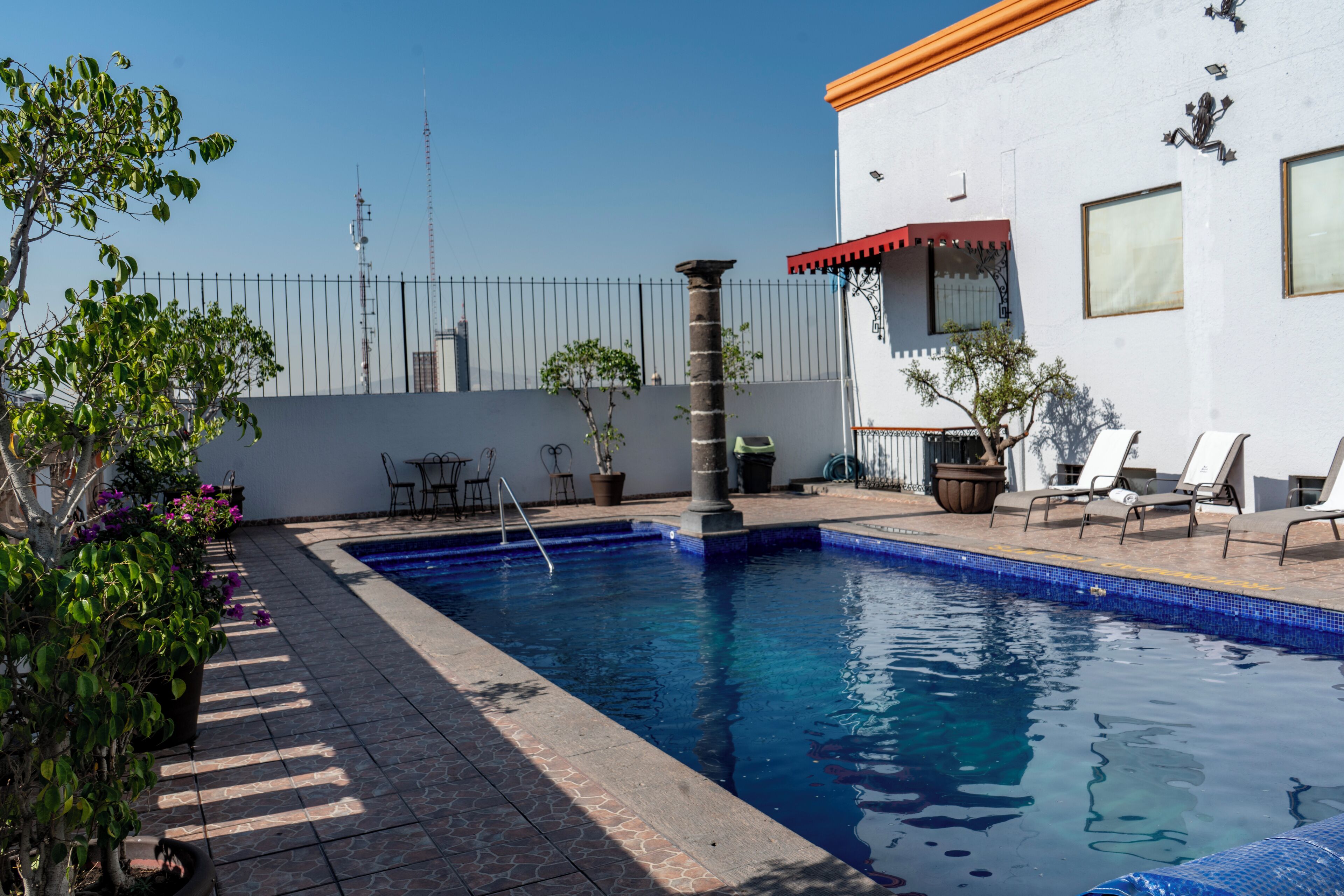 A swimming pool with a tiled deck, surrounded by potted plants and outdoor furniture.