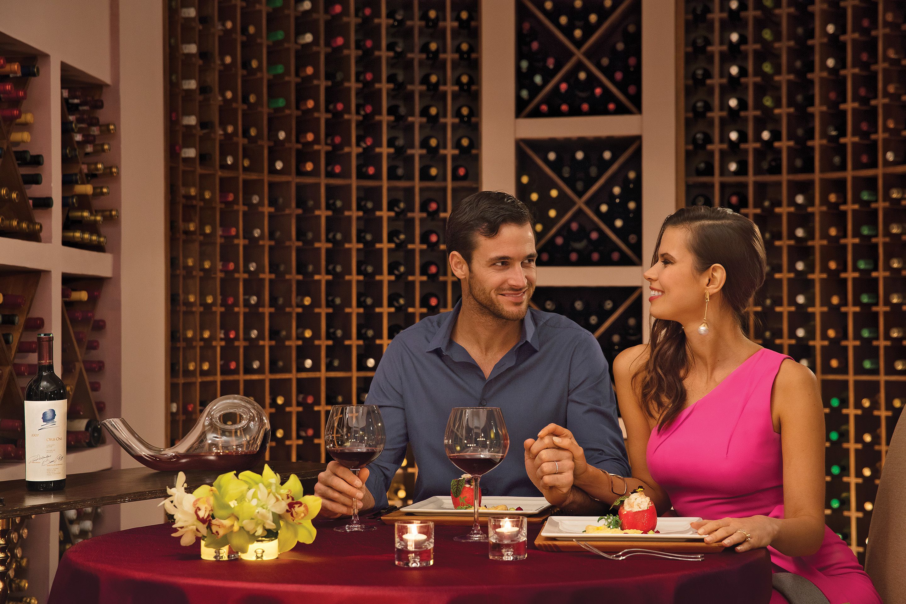 A couple dining at a table with wine glasses, a bottle of wine, and a fruit dish.
