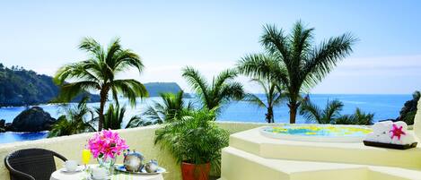 A terrace with a table set for two, overlooking a coastal view with palm trees and a clear sky.