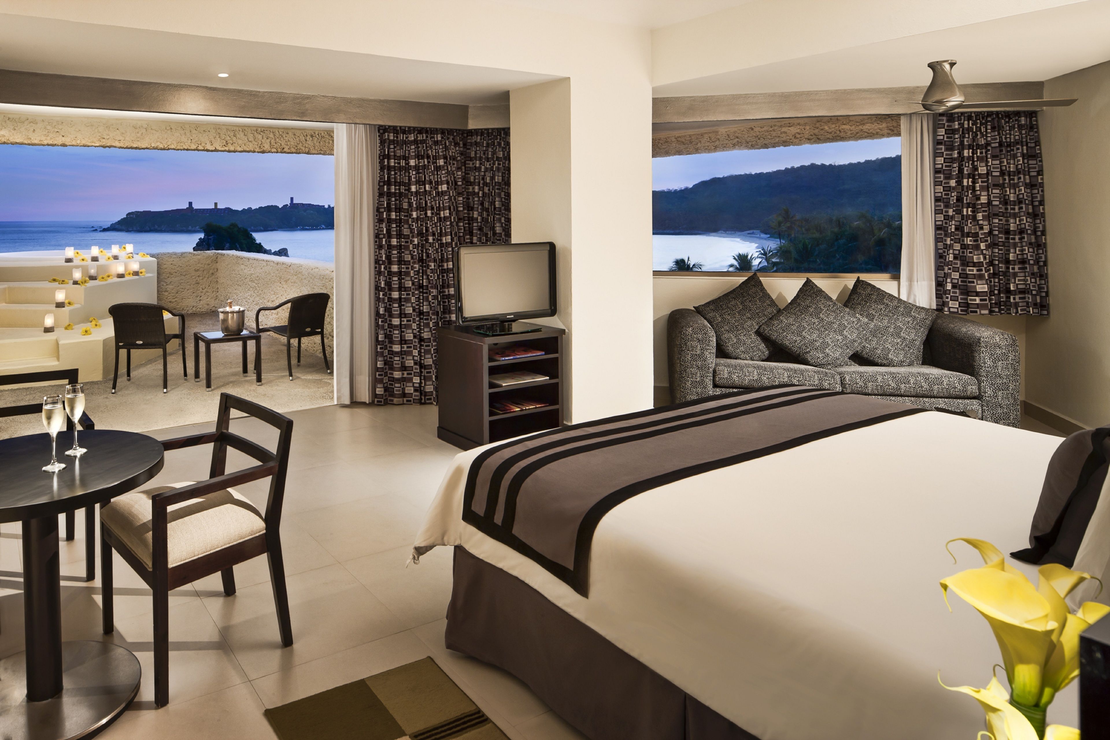 Habitación de hotel con una cama grande, un escritorio con dos sillas, un televisor y vistas al mar.