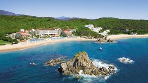 A coastal resort with multiple buildings, a sandy beach, and rocky outcrops in the water. - Dreams Huatulco Resort & Spa - All Inclusive (Santa María Huatulco)