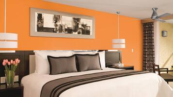 Una habitación de hotel moderna con una cama grande, un ventilador de techo y una obra de arte enmarcada sobre la cama.