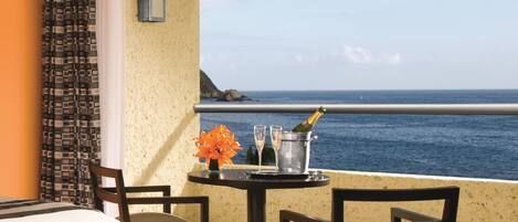 A hotel room with a balcony, a bed, a table with a bottle of champagne, and a view of the sea.