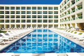 Un hotel con una piscina grande, varios balcones y tumbonas.