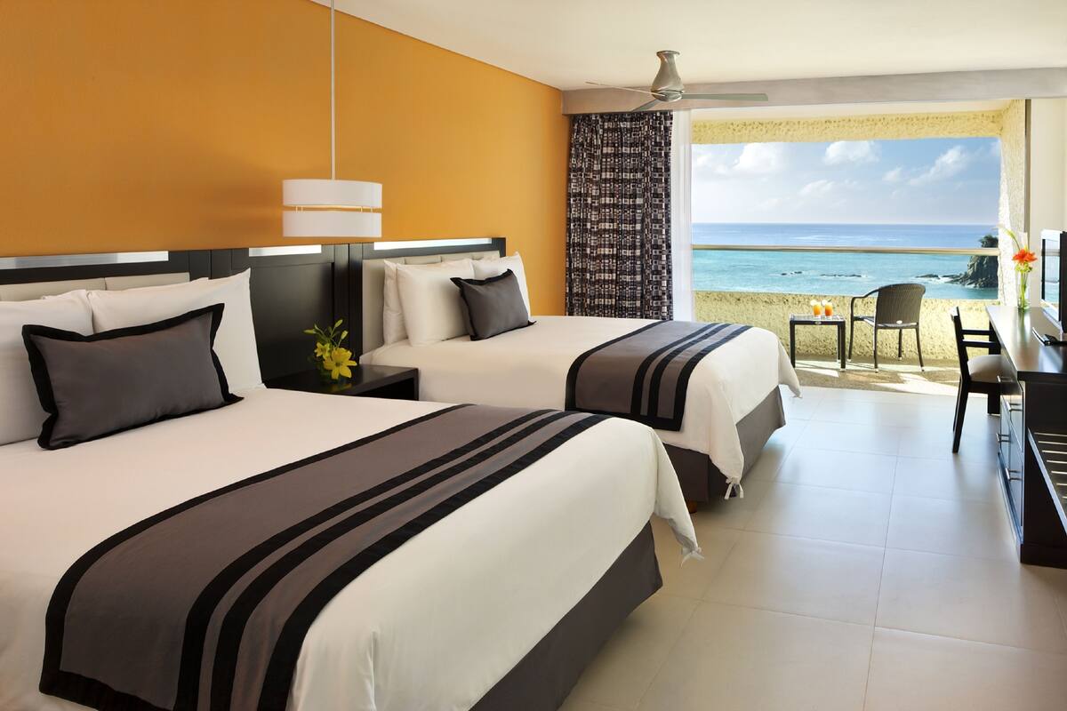 Ein Hotelzimmer mit zwei Betten, einem Schreibtisch und Blick auf den Strand.