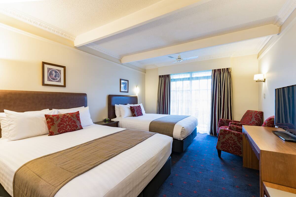 A hotel room with two beds, a desk, a chair, and a television.