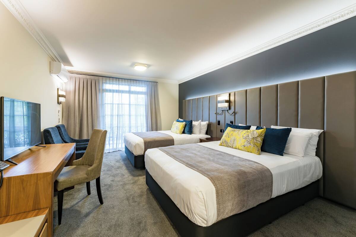 A hotel room with two beds, a desk, a chair, a television, and a window with curtains.