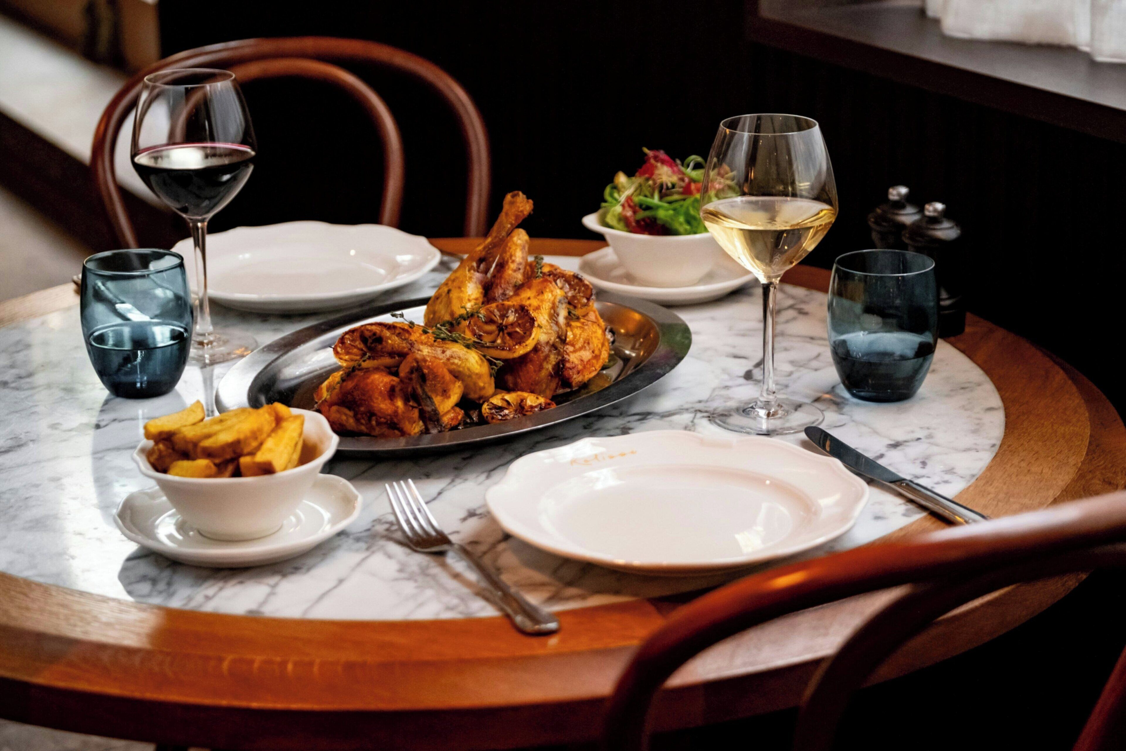 A dining table with a roasted chicken, salad, and wine glasses.