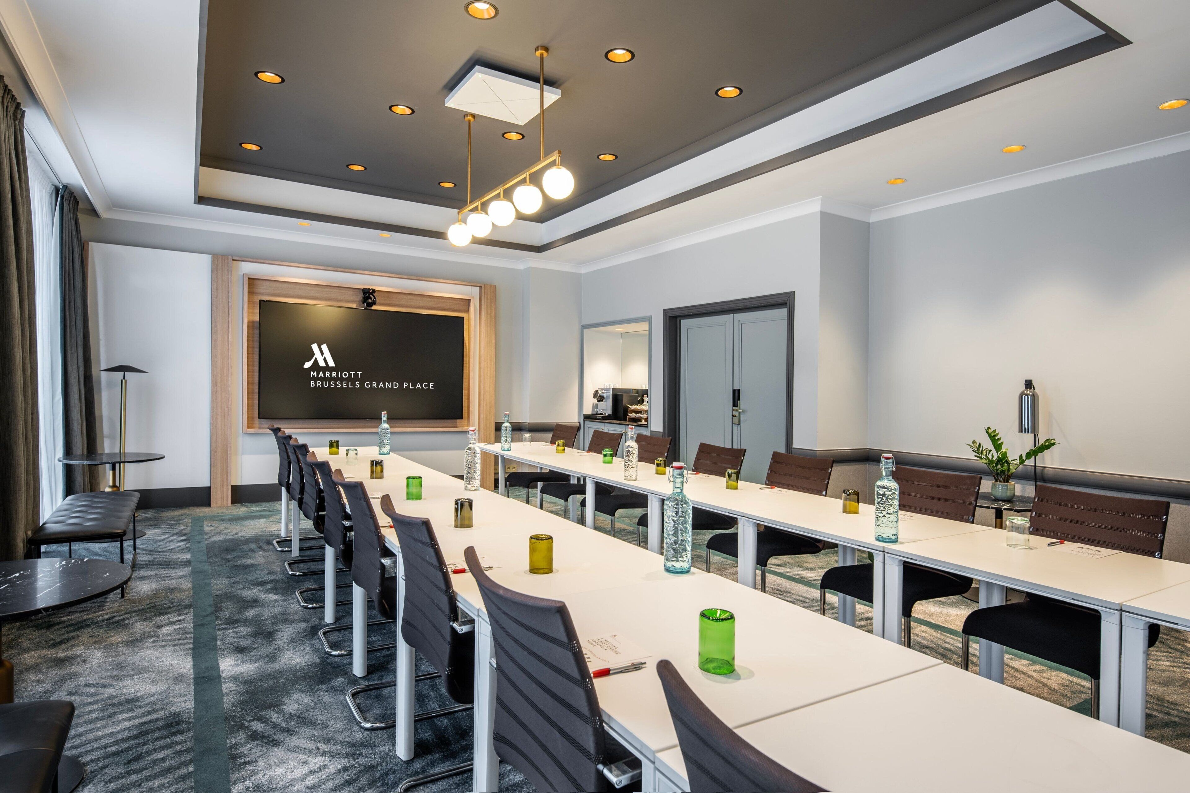 A modern conference room with a long table, black chairs, and a large screen displaying the hotel name.