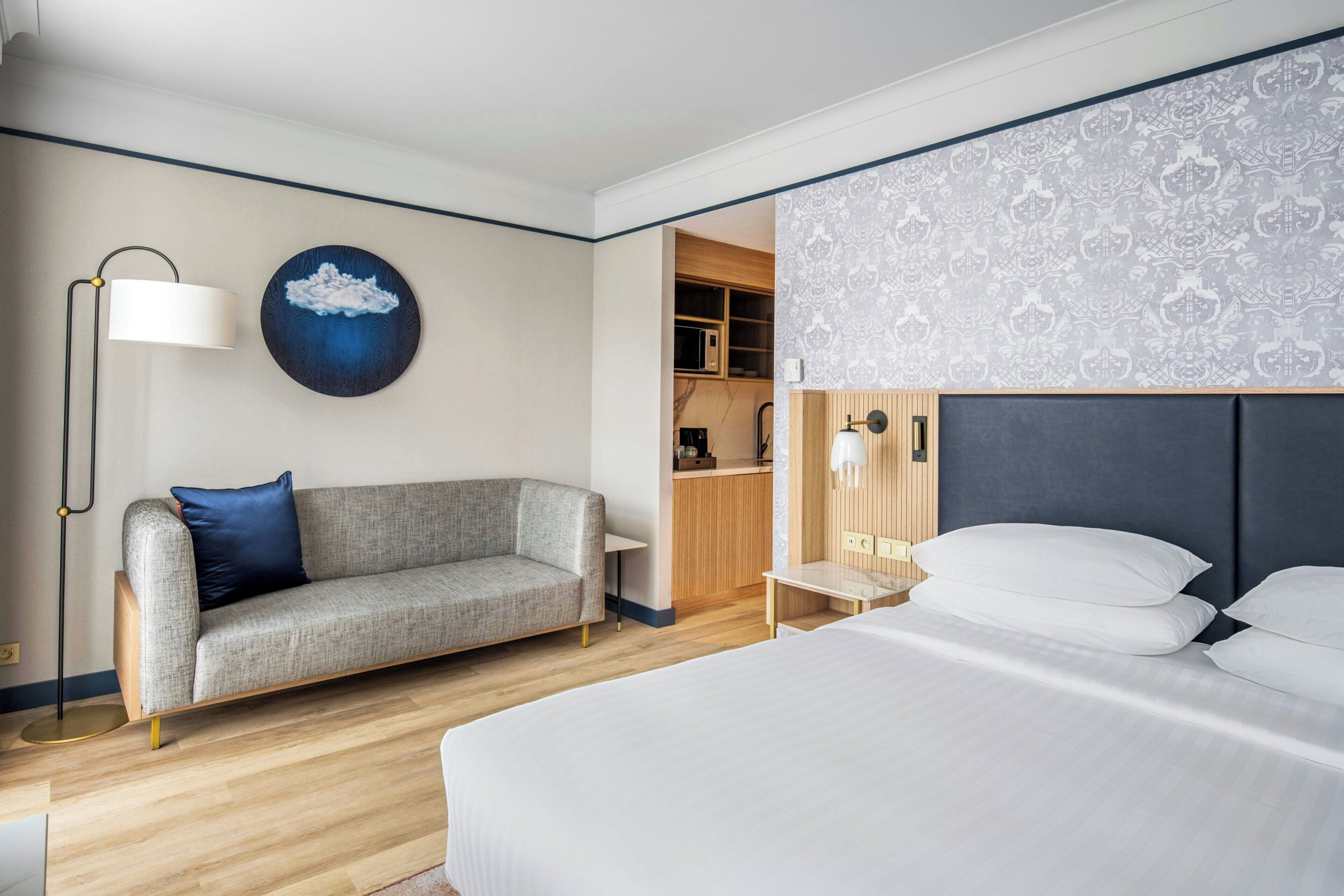 Une chambre d’hôtel comprenant un lit, un canapé, un bureau, une lampe, une œuvre d’art accrochée au mur et un coin cuisine.