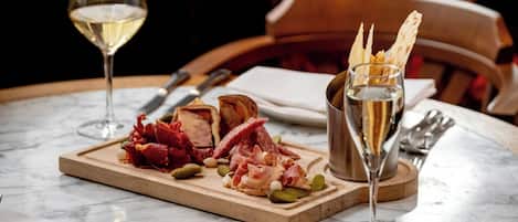 Un tavolo in marmo con un tagliere di salumi, un bicchiere di vino bianco e un bicchierino.