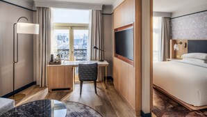 Habitación de hotel con cama, escritorio, silla y un ventanal con vista a la ciudad.