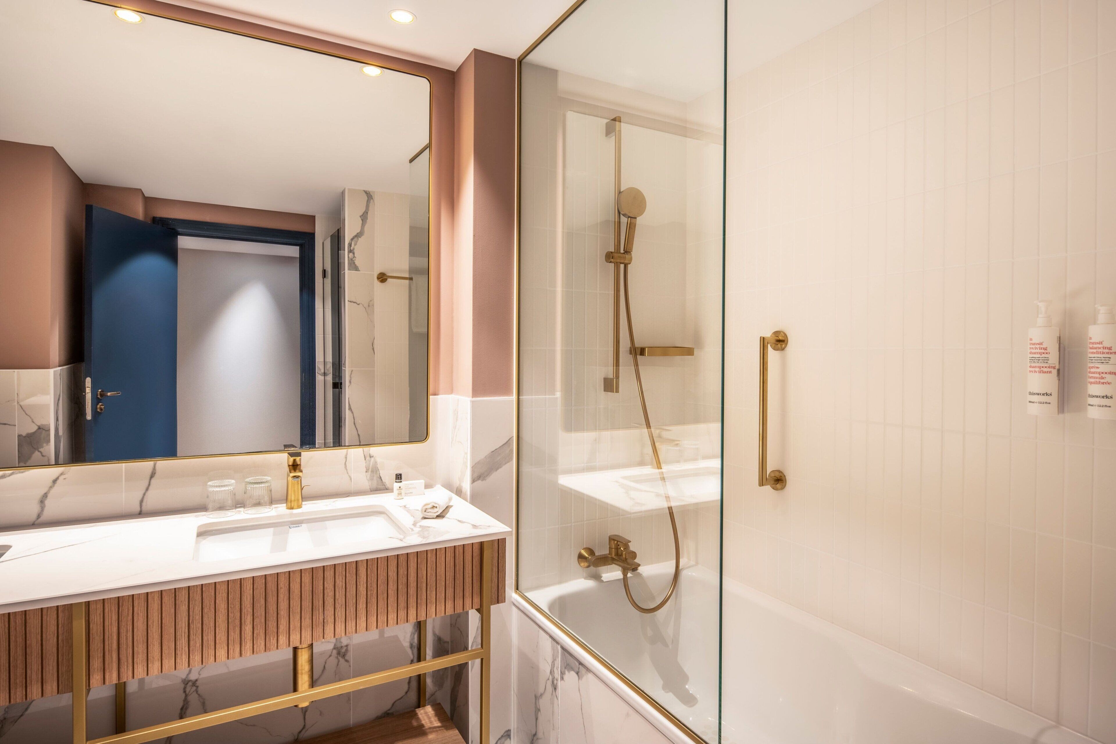 Une salle de bain moderne dotée d’une douche à parois de verre, d’un meuble-lavabo avec un plan de travail en marbre et d’un grand miroir.
